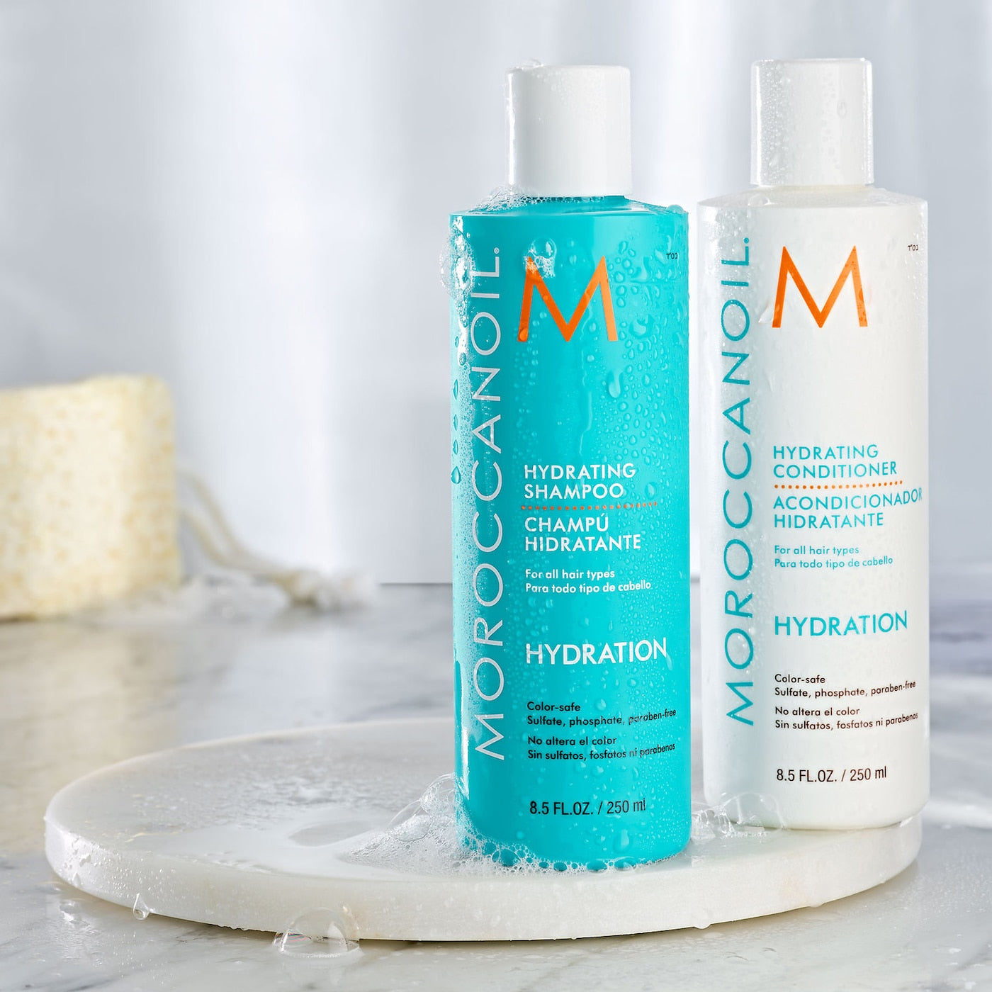 Moroccanoil Hydrating Shampoo and Conditioner bottles on a marble surface with a neutral background.
