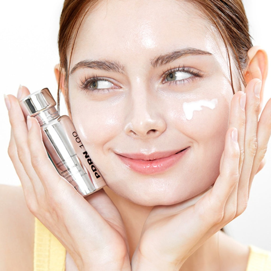 Woman holding a skincare vt pdrn with a close-up of her face, showing a smooth texture.