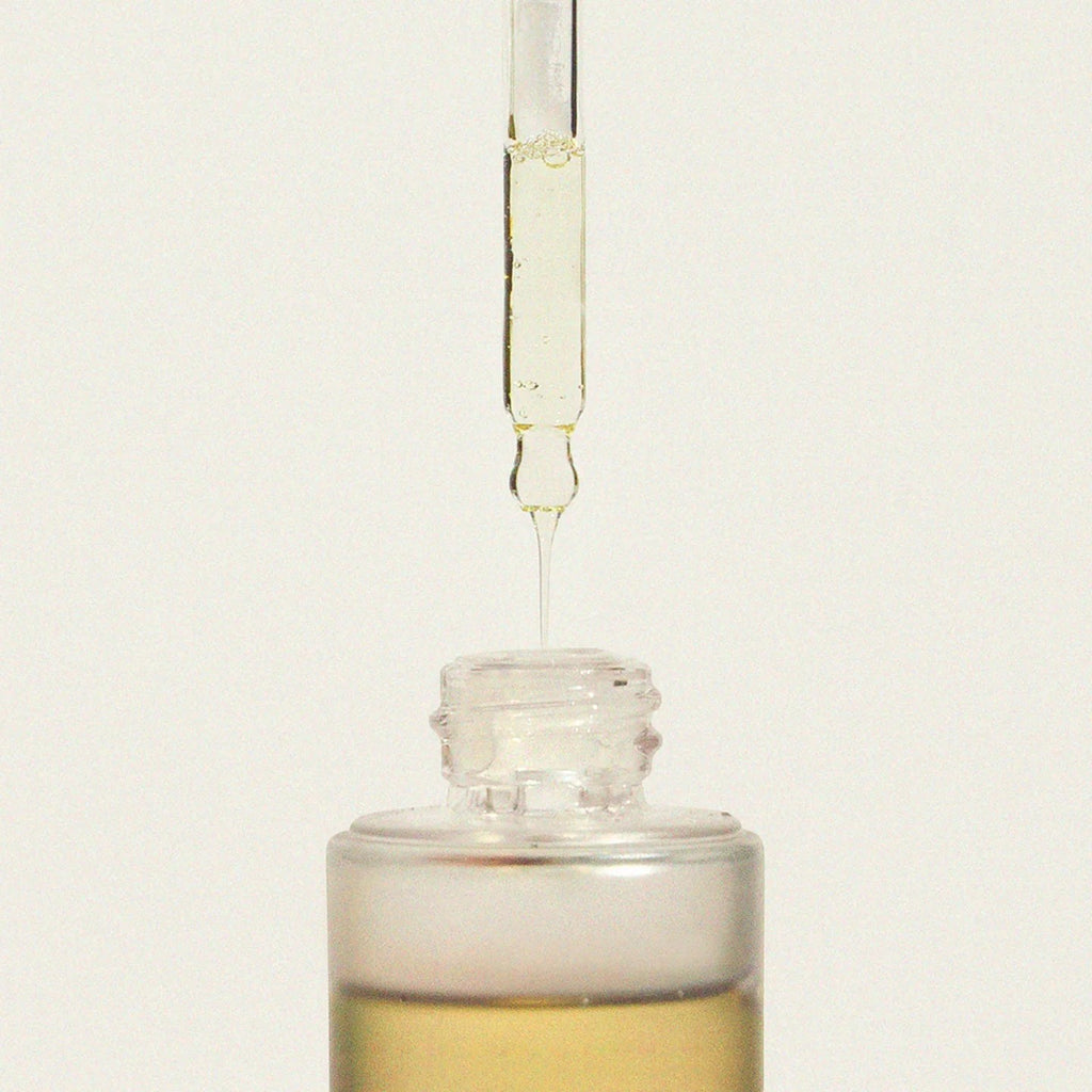 Glass dropper bottle with liquid being dispensed on a light beige background