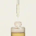 Glass dropper bottle with liquid being dispensed on a light beige background
