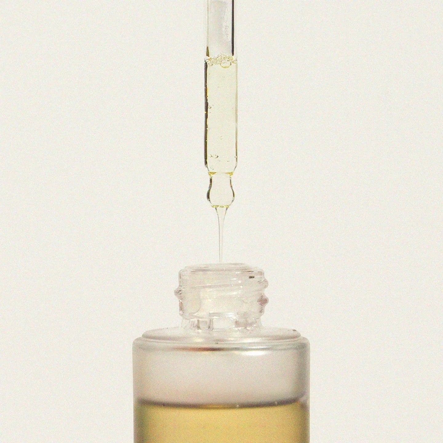 Glass dropper bottle with liquid being dispensed on a light beige background